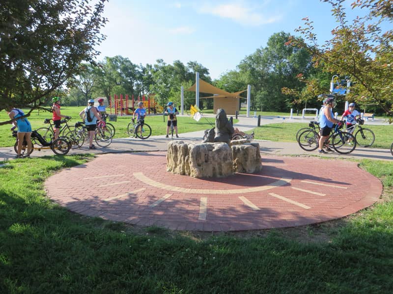 Bicyclists riding around a brick plaza with a bronze sculpture in the middle